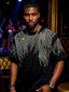 Man wearing a black t-shirt with silver feather designs in a dimly lit indoor setting.