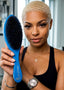 A woman with a short blonde haircut holds up a blue hairbrush with black bristles. The brush has the brand name 'SIR STYLES' printed on the handle.