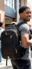 A man wearing a black On Stylus backpack with red accents, photographed outdoors on a campus-style walkway.