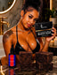 A woman in a black lingerie top holds a black box labeled 'RAW ORGANIC AFRICAN BLACK SOAP' next to a dark dropper bottle and three dark soap bars on a marble countertop in a bathroom setting.