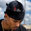 A man wearing a black velvet durag headwrap with a red and white 'SPI STYLES' logo, photographed outdoors against a cloudy blue sky.