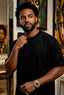 Man wearing a black speckled shirt and gold watch in an art gallery setting