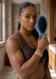 Woman holding a blue hairbrush in a room with neutral decor