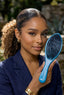 Woman holding a blue hairbrush with a blurred outdoor background