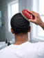Person using a red and white hairbrush on their styled hair in a bathroom setting