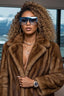 Woman wearing a brown fur coat and blue sunglasses with a blurred background