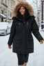 Person wearing a black parka with a fur-lined hood in a snowy urban setting