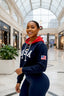 Woman wearing a navy blue 'USA' sweatshirt with an American flag patch in a mall setting.