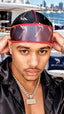 A man wearing a black and red 'Saints Style' durag cap, posing on a yacht with a marina and city skyline in the background.