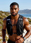 Muscular man wearing a black athletic vest outdoors with a scenic background