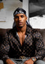 Man wearing a patterned shirt and cap sitting on a couch.