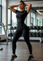 Woman in a gym wearing a black outfit with visible branding.