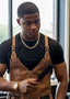 Man wearing a brown leather apron holding a brush, with a blurred indoor background.