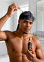 Man holding a dropper bottle and a bottle of hair oil in a bathroom setting